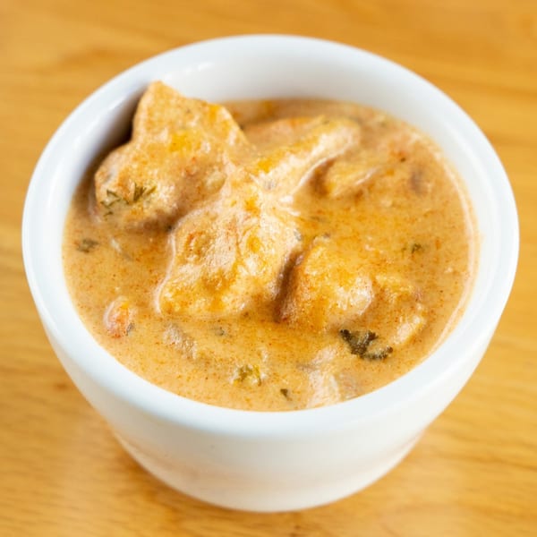 A white bowl filled with creamy, orange-colored Brazilian chicken stroganoff on a wooden table.