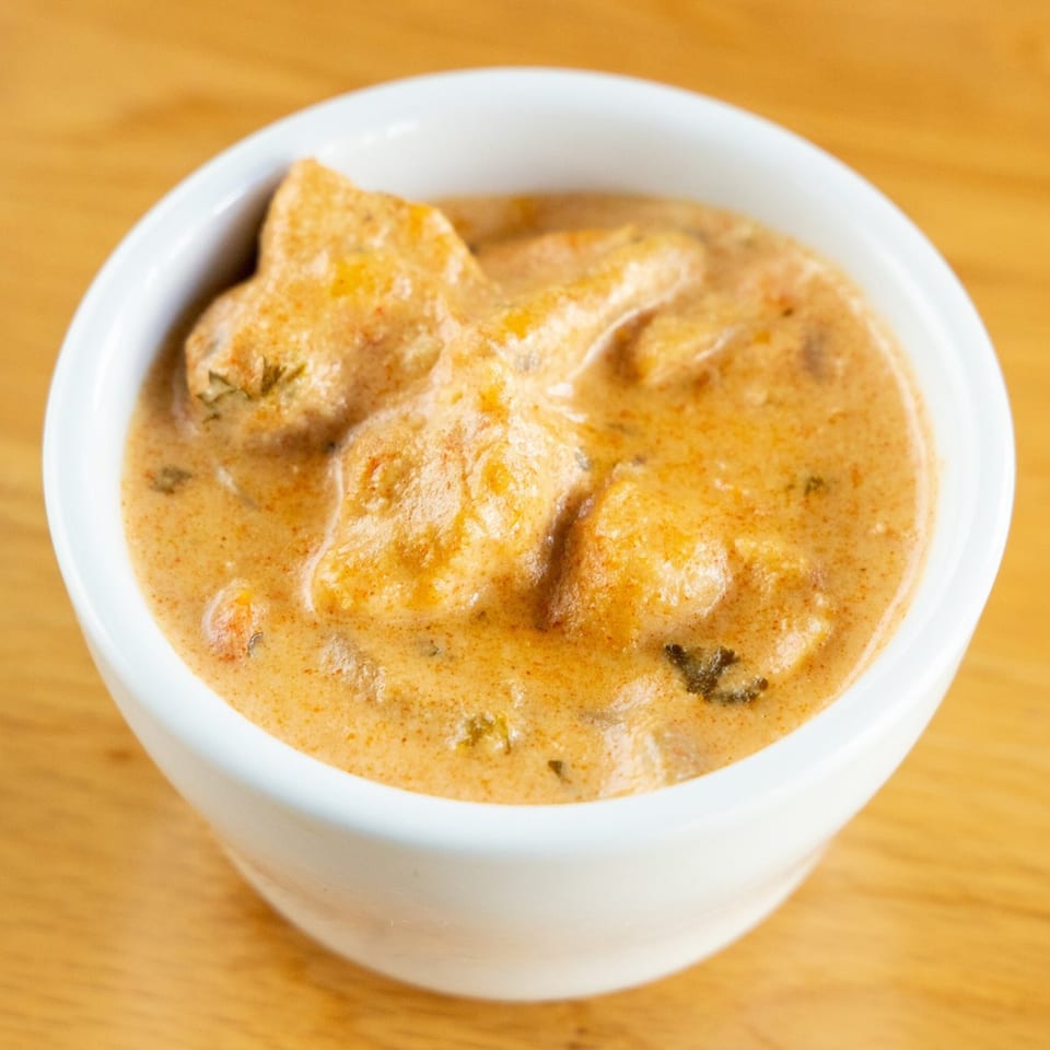 A white bowl filled with creamy, orange-colored Brazilian chicken stroganoff on a wooden table.