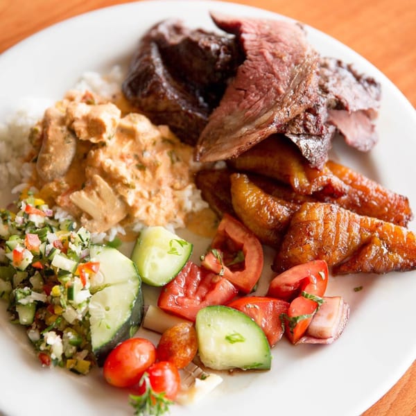 A Brazilian plate with grilled steak, rice, creamy chicken, fried plantains, and fresh salad.