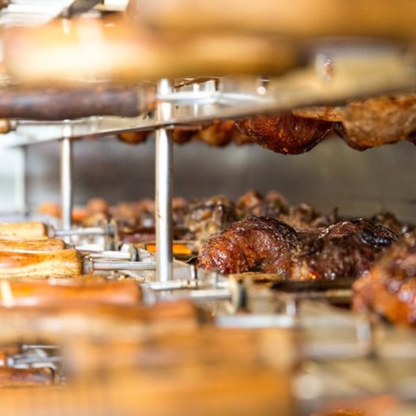 Brazilian churrasco grill with various cuts of meat and sausages cooking on rotating skewers.