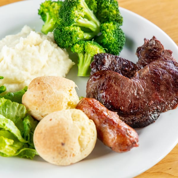 A Pampas Grill plate with steak, sausage, mashed potatoes, broccoli, cheese bread, and lettuce.