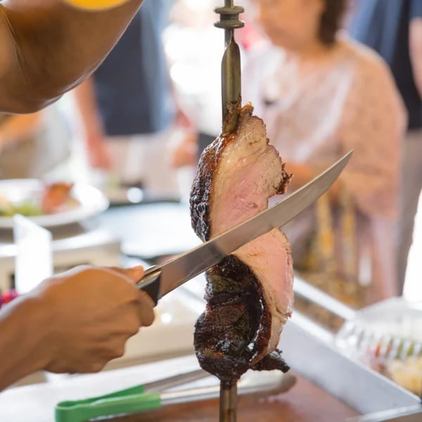 A server at Pampas Grill carves a slice of picanha from a large skewer.