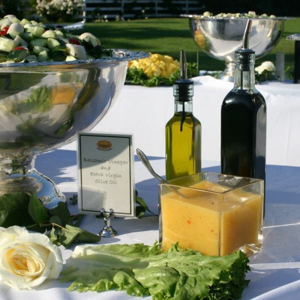 Outdoor buffet table with salad, olive oil, balsamic vinegar, and a creamy dressing.