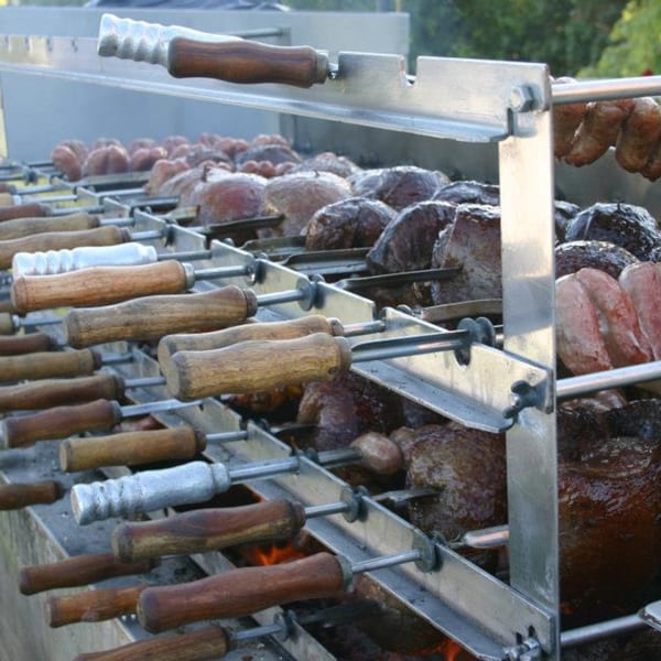 Brazilian churrasco grill with various meats and sausages cooking over an open flame.