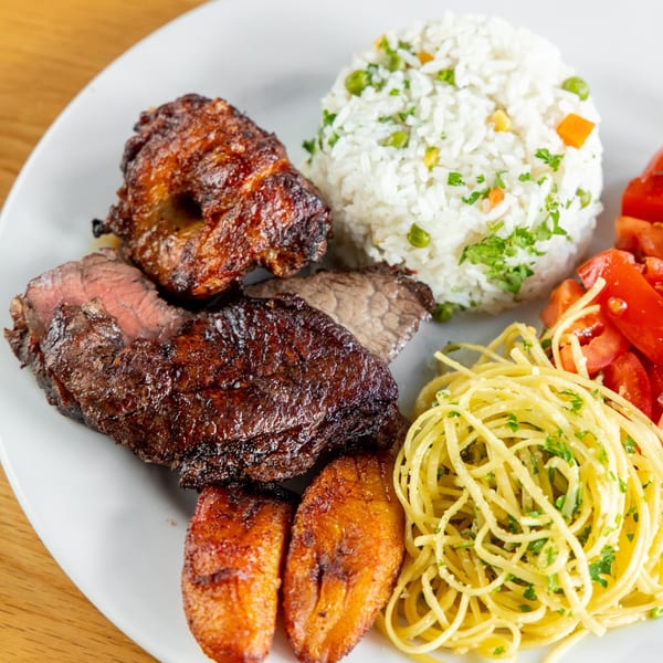 A Pampas Grill plate with grilled meats, rice, spaghetti, fried plantains, and diced tomatoes.