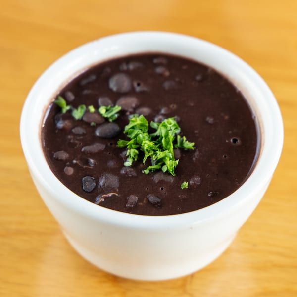 A white bowl filled with dark Brazilian black bean soup, garnished with fresh green parsley.