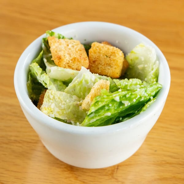 A small white bowl filled with fresh Caesar salad, topped with croutons and parmesan cheese.