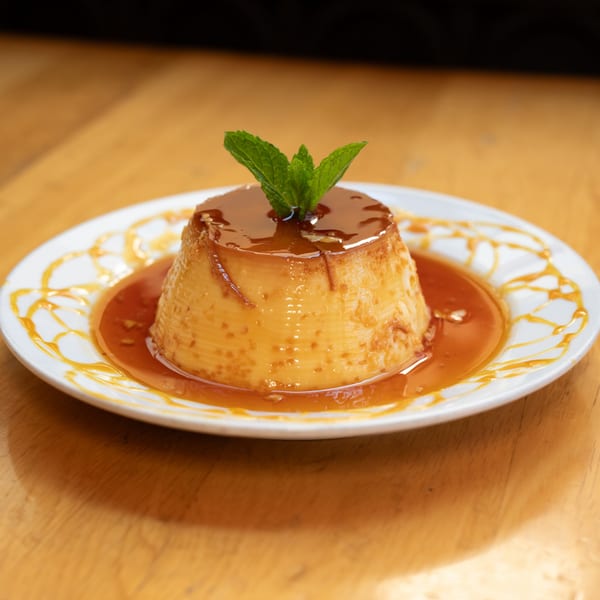 Brazilian flan dessert with caramel sauce and a mint garnish on a white plate.