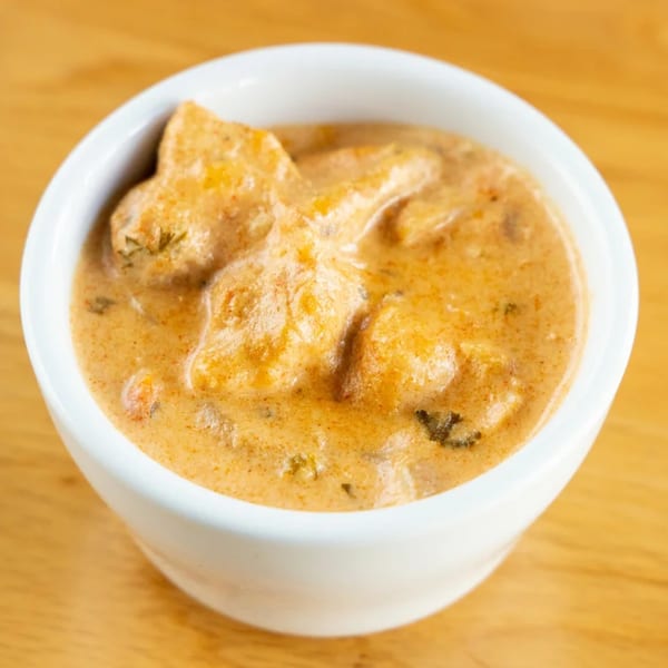 A white bowl filled with a creamy, light orange Brazilian chicken stroganoff on a wooden table.