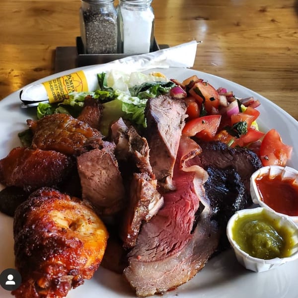A plate of Pampas Grill's Brazilian barbecue with various meats, salad, and two dipping sauces.