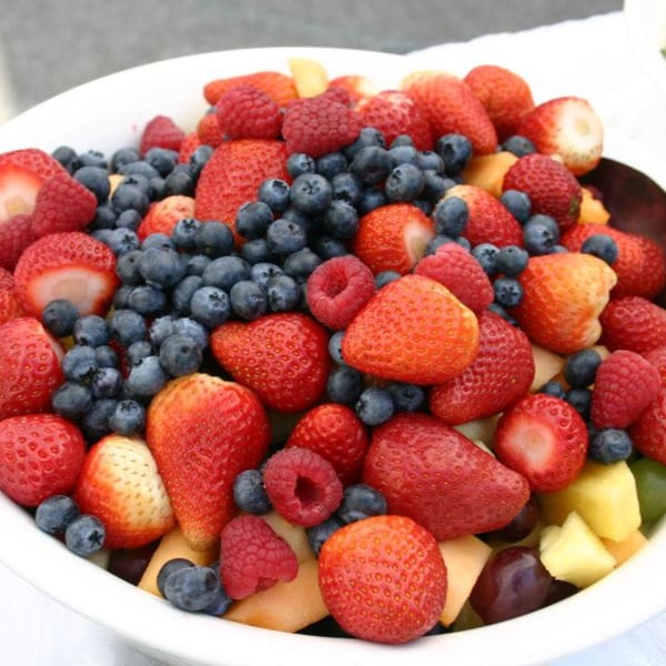 A large white bowl filled with fresh strawberries, blueberries, raspberries, and other fruit.