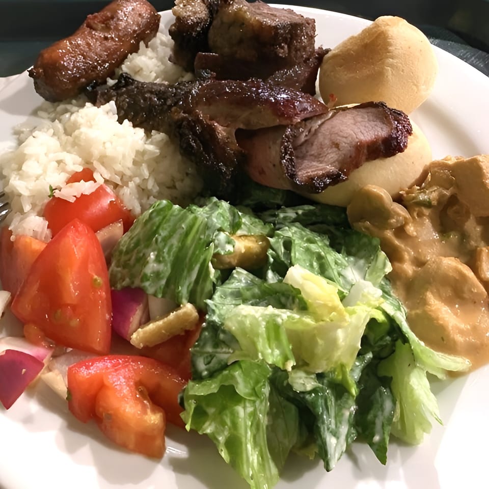 A Brazilian plate with rice, grilled meats, bread, tomato salad, green salad, and a creamy sauce.