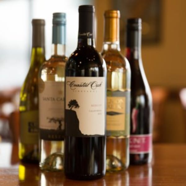 Five bottles of red and white wine, including Coastal Oak and Santa Carolina brands, on a wooden table.