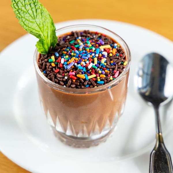 Brazilian chocolate dessert with colorful sprinkles and a mint leaf in a glass on a white plate.