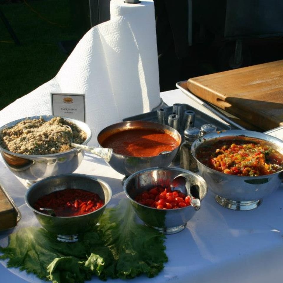 A buffet spread of Brazilian farinha, sauces, and salsa in silver bowls on a white tablecloth.