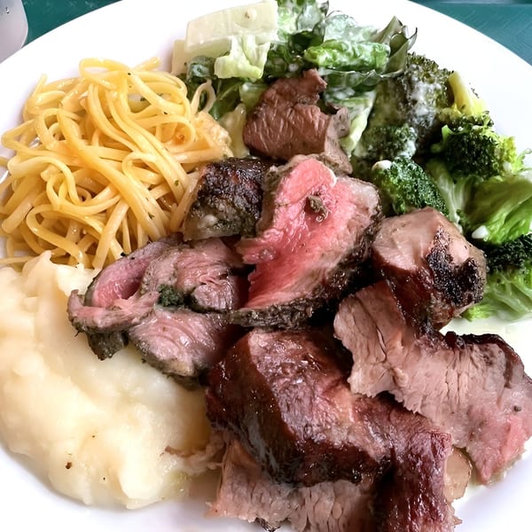 A Pampas Grill plate with sliced steak, mashed potatoes, pasta, and a salad with broccoli.