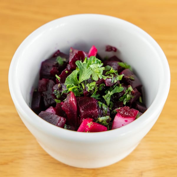 A white bowl filled with diced beets and fresh green herbs on a wooden surface.