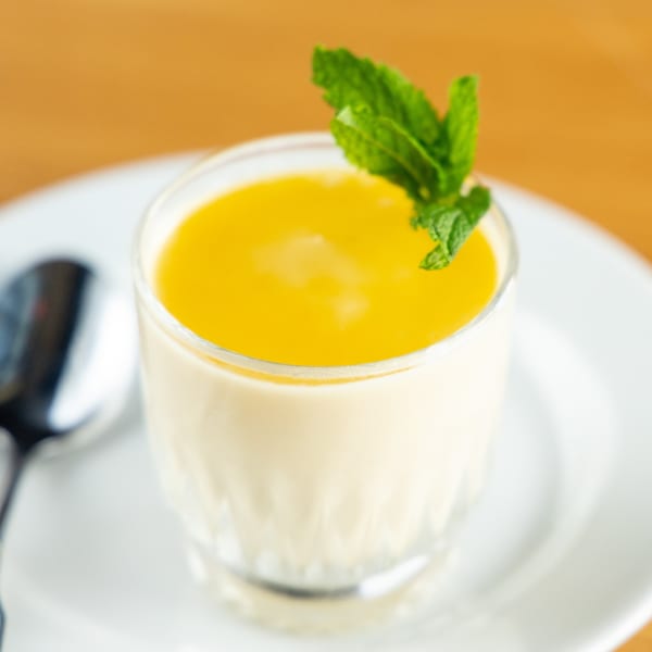 Brazilian passion fruit mousse dessert in a glass, garnished with mint, on a white plate.